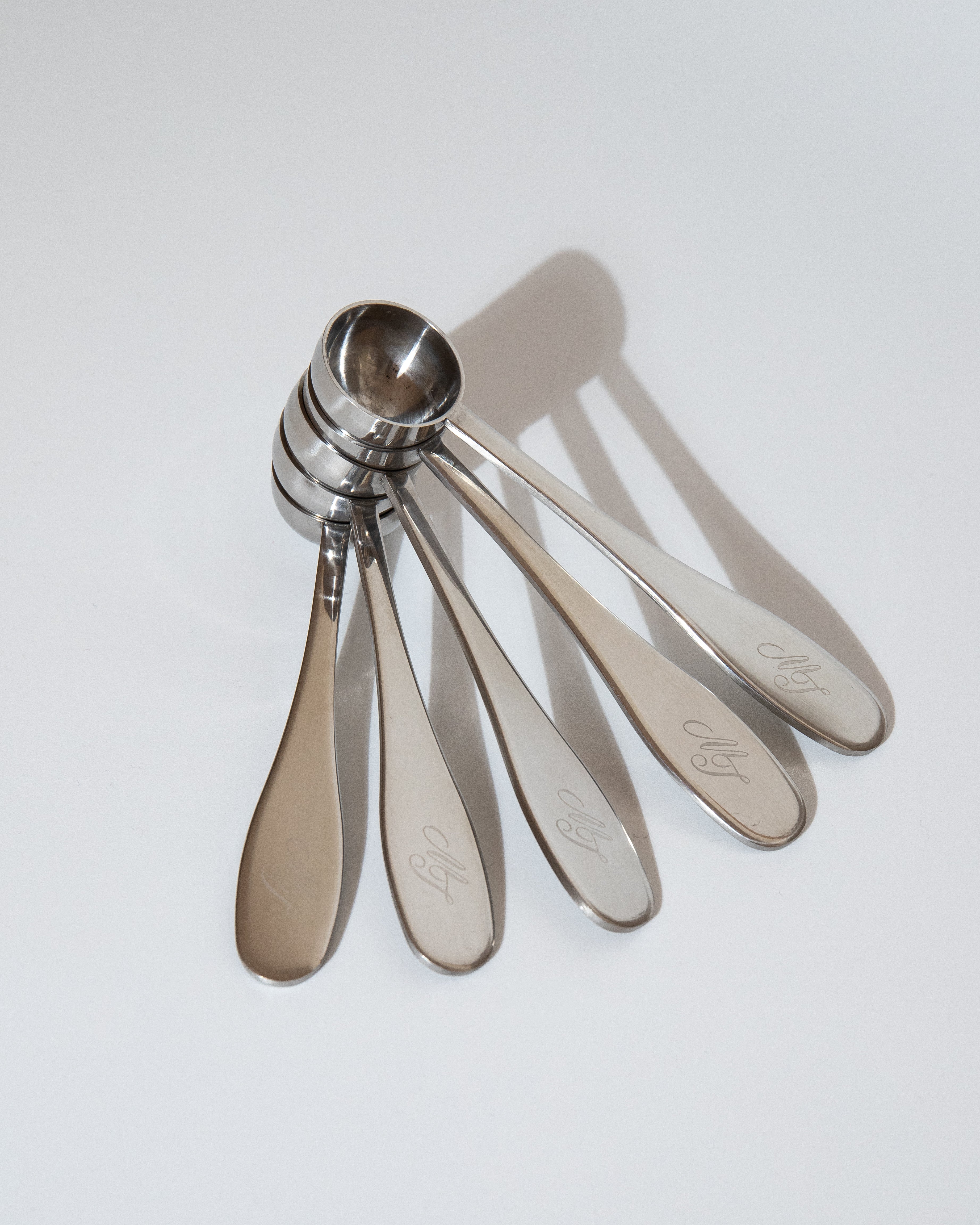 Set of five metal measuring spoons on a light gray background